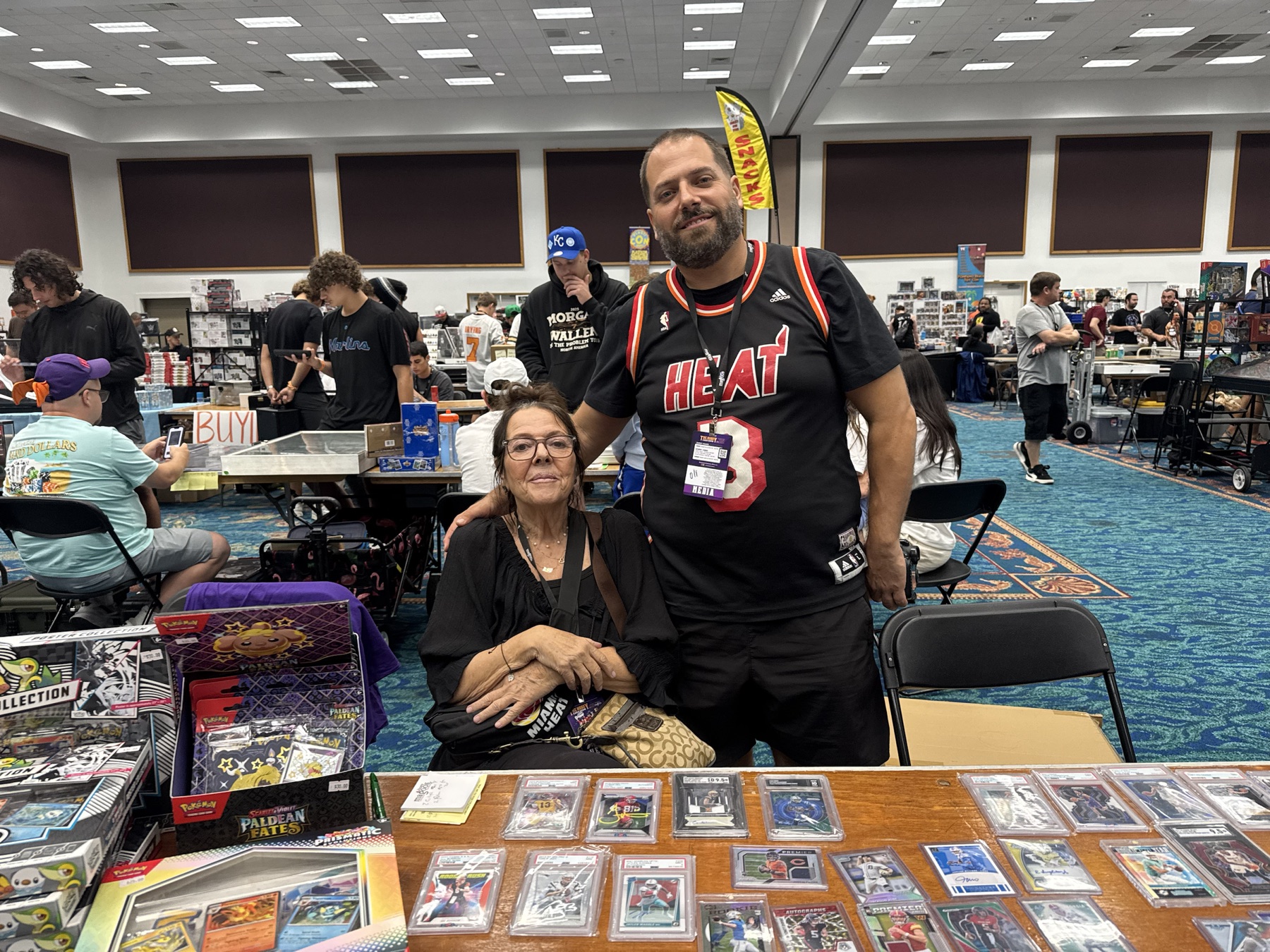 OLI SPORTCARDZ at a busy card-show table filled with trading cards